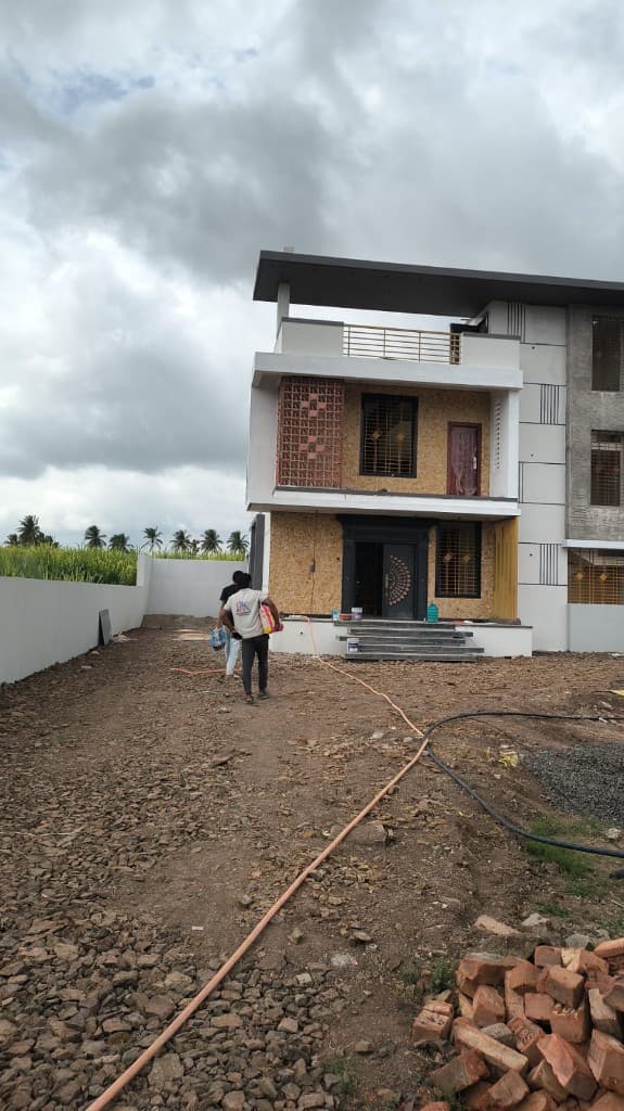 KM Construction two-storey residence during finishing works, with jaali screen and site crew